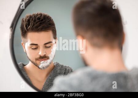 Schöner junger Mann, der sich in der Nähe des Spiegels im Bad rasieren kann Stockfoto