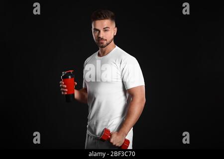 Sportlicher Mann mit Proteinshake und Hantel auf dunklem Hintergrund Stockfoto