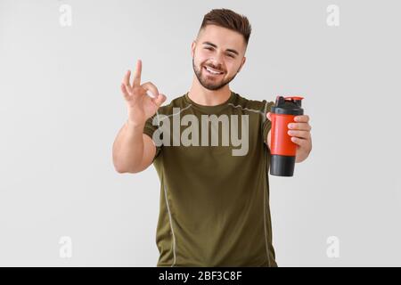 Sportlicher Mann mit Proteinshake zeigt OK auf hellem Hintergrund Stockfoto