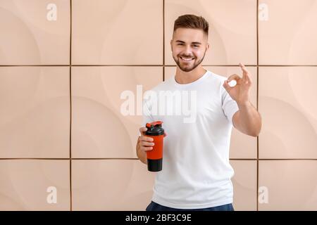 Sportlicher Mann mit Protein-Shake zeigt OK auf farbigen Hintergrund Stockfoto