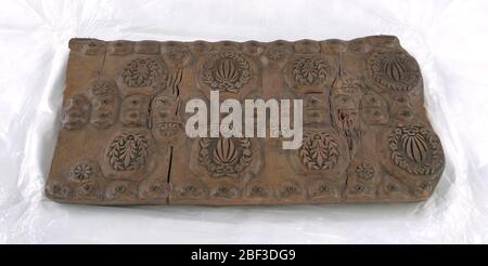 Holzblock. Rechteckiger Block bestehend aus drei Schichten Holz, von denen die obere geschnitzt ist. Zwei Paare von großen und zwei Paare von kleineren Kränzen zentrieren Blätter. Doppelreihe mit kleinen Baumstäben und Punkten, in Messing, durchgangszentriert und eine Reihe oben und unten. Stockfoto