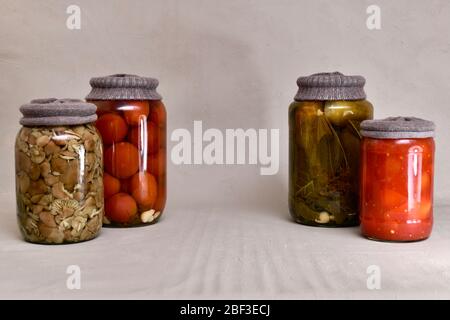 Glasgefäße mit Textil, mit fermentierten Gurken, Tomaten, Pilzen und Paprika, zwei Dosen auf beiden Seiten. Stockfoto