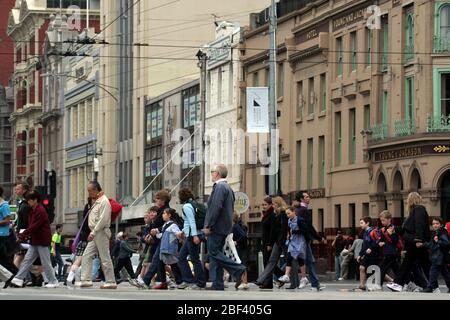 FUSSGÄNGER, DIE EINE STARK BEFAHRENE KREUZUNG IN MELBOURNE, VICTORIA, AUSTRALIEN ÜBERQUEREN. Stockfoto