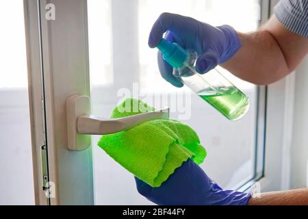 Mann desinfiziert Türgriff mit Desinfektionsflüssigkeit. Türgriff sprühen und mit einem Tuch abwischen. Desinfektion von Räumlichkeiten.Prävention Coronavirus, in Stockfoto