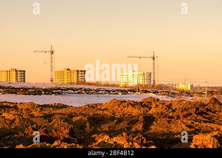 Ein Haufen ausgegrabener Erde, um das Gelände vor dem Neubau in der Ferne zu ebnen, werden mehrstöckige Gebäude mit Turmkranen gebaut Stockfoto