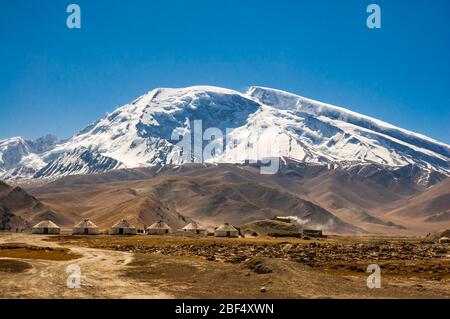 Konkrete touristische Jurten am Rande der See Karakul mit Muztagata Berg hinter, Provinz Xinjiang, China Stockfoto