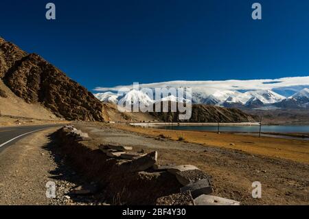 Wolke bedeckt Berge im Bereich von Pamir mit dem Karakorum Highway schlängelt um Kakakul See im Vordergrund. Xinjiang Stockfoto