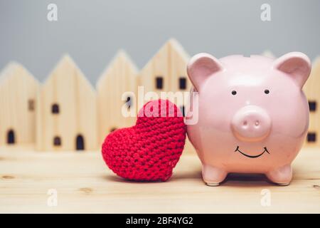 Nettes Schwein Lächeln mit rotem Herz auf Heimatdorf Hintergrund für Liebe Gemeinschaft sicheres Haus Konzept. Stockfoto