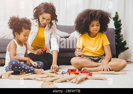 Alleinerziehende Mutter lebt mit zwei Tochter, die Puzzle-Spielzeug in der Wohnung lernt und spielt. Nanny suchen oder Kinderbetreuung im Wohnzimmer schwarze Menschen. Stockfoto