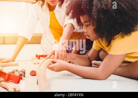 Alleinerziehende Mutter lebt mit zwei Tochter, die Puzzle-Spielzeug in der Wohnung lernt und spielt. Nanny suchen oder Kinderbetreuung im Wohnzimmer schwarze Menschen. Stockfoto