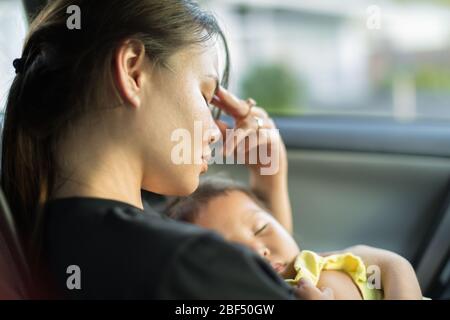 Eine unglückliche erschöpfte Mutter, die versucht, ein Nickerchen mit ihrem Baby im Auto zu machen. Stockfoto