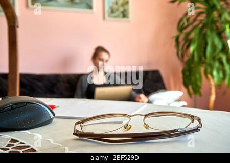 Gläser auf dem Tisch. Junge Frau, die mit Laptop im Hintergrund arbeitet. Stockfoto