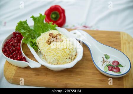 Traditioneller russischer Salat Mimoza. Isoliert auf Holzhintergrund. Draufsicht. HÜHNERSALAT mit Walnüssen und Pilzen. Granatapfel aus Granulat Stockfoto