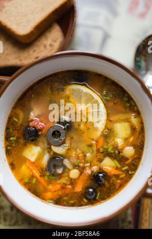 Keramikplatte mit Suppe Soljanka, russische Hodgepodge-Suppe mit Oliven und Zitrone Stockfoto