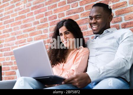 Porträt von ein glückliches junges Paar sitzt auf der Couch mit Laptop Stockfoto