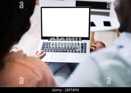 Schönes junges Paar, das Seite an Seite auf EINEM Sofa sitzt und zusammen EINEN Laptop anschaut Stockfoto
