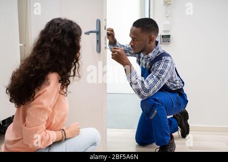 Lächelnde Frau an Techniker zur Festsetzung der Seitentür mit einem Schraubendreher zu Hause Suchen Stockfoto