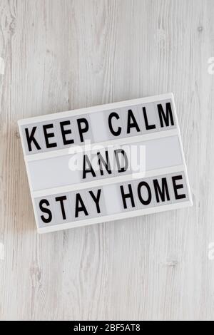 „Keep Calm and Stay Home“-Worte auf einem modernen Brett auf einer weißen Holzfläche, Draufsicht. Über Kopf, von oben, flach gelegt. Stockfoto