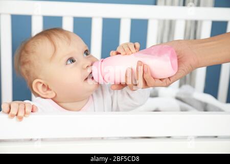 Mutter füttert Baby mit Milch aus der Flasche im Schlafzimmer Stockfoto