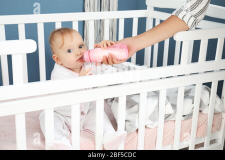 Mutter füttert Baby mit Milch aus der Flasche im Schlafzimmer Stockfoto