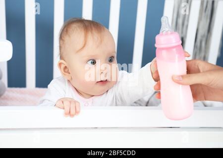 Mutter füttert Baby mit Milch aus der Flasche im Schlafzimmer Stockfoto