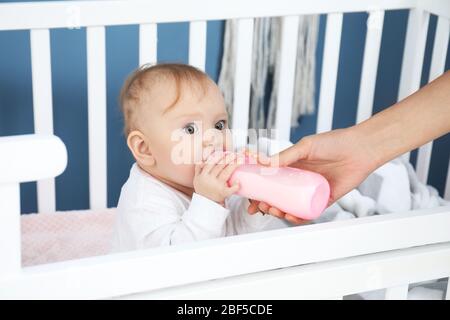 Mutter füttert Baby mit Milch aus der Flasche im Schlafzimmer Stockfoto