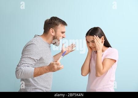 Emotional junges Paar mit Schwangerschaftstest auf farbigem Hintergrund Stockfoto