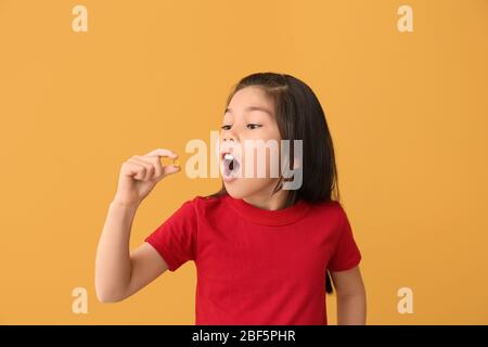 Kleines Mädchen, das Fischölpille vor Farbhintergrund nimmt Stockfoto