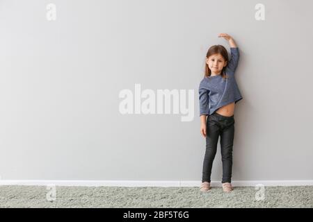 Kleines Mädchen misst Höhe in der Nähe von grauen Wand Stockfoto