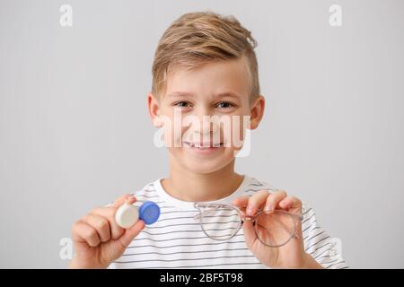 Kleiner Junge mit Kontaktlinsenhülle und Brille auf grauem Hintergrund Stockfoto