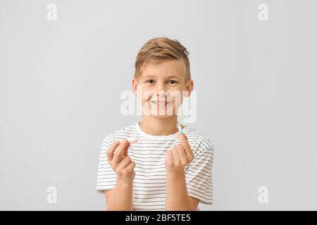 Kleiner Junge mit Kontaktlinsenhülle und Pinzette auf grauem Hintergrund Stockfoto