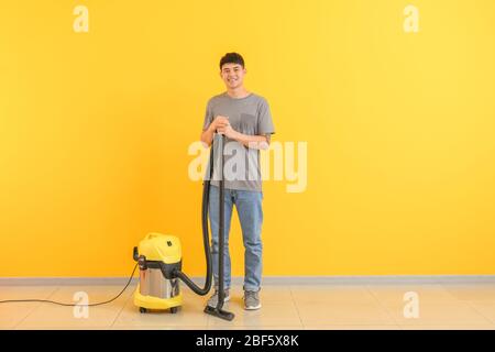 Asiatischer Hausmeister mit Staubsauger in der Nähe von Farbwand Stockfoto