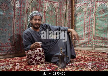 Beduinen in traditioneller Kleidung trinken Tee auf einem Teppich in der saudischen Wüste, Saudi-Arabien Stockfoto