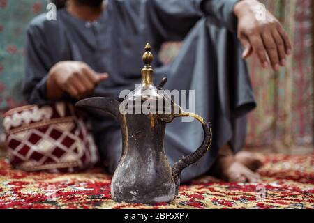 Nahaufnahme der traditionellen arabischen Teekanne mit Beduinen in traditioneller Kleidung auf einem Teppich in der saudischen Wüste, Saudi-Arabien Stockfoto