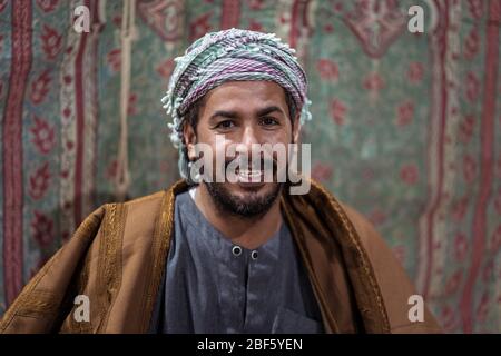 Porträt eines Beduinen-Mannes in traditioneller Kleidung, der mit einem tasbih betet, während er nachts in der saudischen Wüste Tee auf einem Teppich trinkt Stockfoto