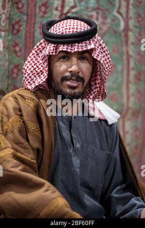 Porträt eines Beduinen-Mannes mit traditionellem Kopftuch auf einem Teppich in der saudischen Wüste, Saudi-Arabien Stockfoto