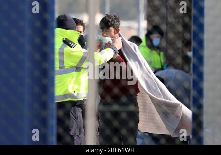 Ein Grenztruppen-Offizier passt einem Mann, der als Migrant gilt, eine Maske, nachdem er nach Dover, Kent, nach kleinen Bootsvorfällen im Kanal heute Morgen, als Großbritannien weiterhin in der Sperre sitzt, um die Ausbreitung des Coronavirus einzudämmen. Stockfoto