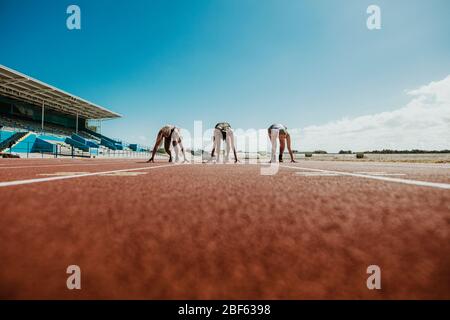 Drei junge Athleten an der Startposition bereit für ein Rennen. Sportfrauen bereit für Rennen auf der Rennstrecke. Stockfoto