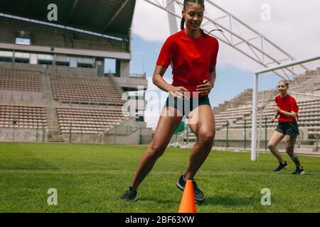 Frauen trainieren auf Fußballplatz. Junger Fußballspieler, der während des Übungspraktik um Kegel im Fußballfeld herumläuft. Stockfoto