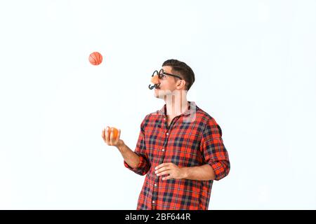 Mann in lustiger Verkleidung jongliert mit Kugeln auf hellem Hintergrund. April Narren Tag Feier Stockfoto