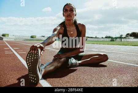 Läuferin macht Dehnungsübungen auf Laufstrecke sitzen. Läuferin sitzt auf Laufstrecke und streckt ihr Bein. Stockfoto