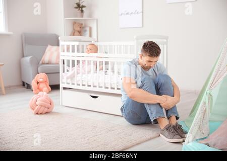 Junger Mann, der an postnataler Depression in der Nähe des Bettes leidet, mit Baby zu Hause Stockfoto