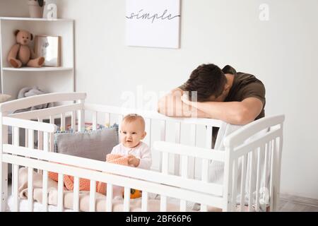 Junger Mann, der an postnataler Depression in der Nähe des Bettes leidet, mit Baby zu Hause Stockfoto