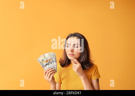 Nachdenkliche junge Frau mit Geld auf farbigen Hintergrund Stockfoto