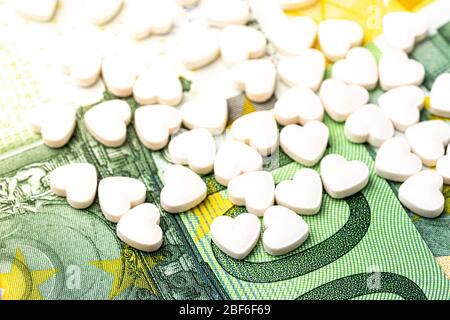 Herzförmige Pillen auf dem Hintergrund der Euro-Rechnungen. Das Konzept der teuren Kosten der Gesundheitsversorgung oder Finanzierung der Medizin. Stockfoto