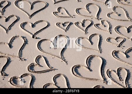 Romantischer Hintergrund handgeschriebener Herzen in glattem Sand an einem sonnigen Strand gezeichnet Stockfoto