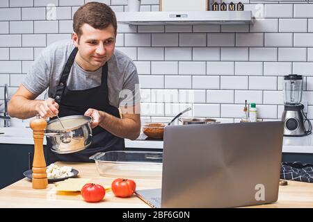 Junger Mann in der Küche auf der Suche nach Rezepten auf seinem Laptop. Stockfoto