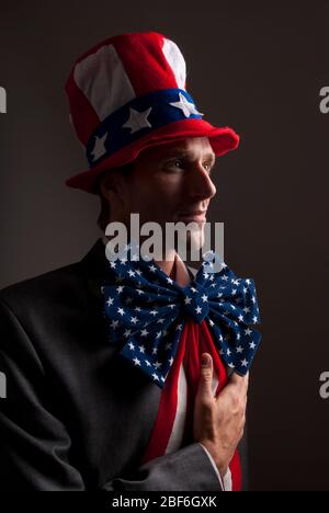 Porträt eines ernsten patriotischen Mannes mit amerikanischen Flaggen Sterne und Streifen Hut und Bogen stehen vor einem dunklen Hintergrund Stockfoto