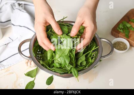 Frau mit frischem Spinat in Sieb auf dem Tisch Stockfoto