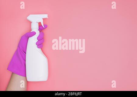 Frau Hand in rosa Gummi Schutzhandschuh hält Reinigungsmittel Flasche auf rosa Hintergrund. Stockfoto